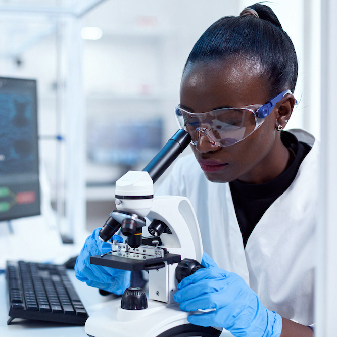 Medical scientist using microscope and conducting research in a sterile laboratory.