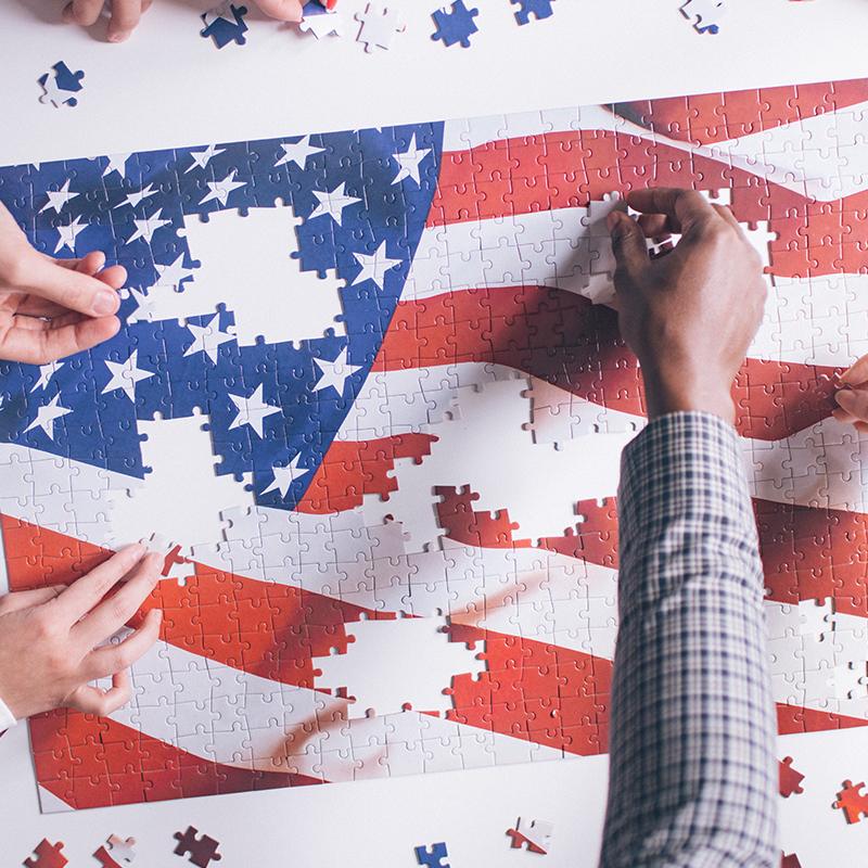 People's hands as they put together a puzzle of the American flag