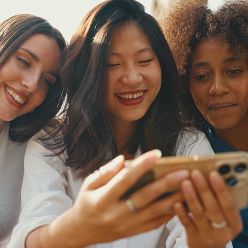 Three smiling women looking at a mobile phone together