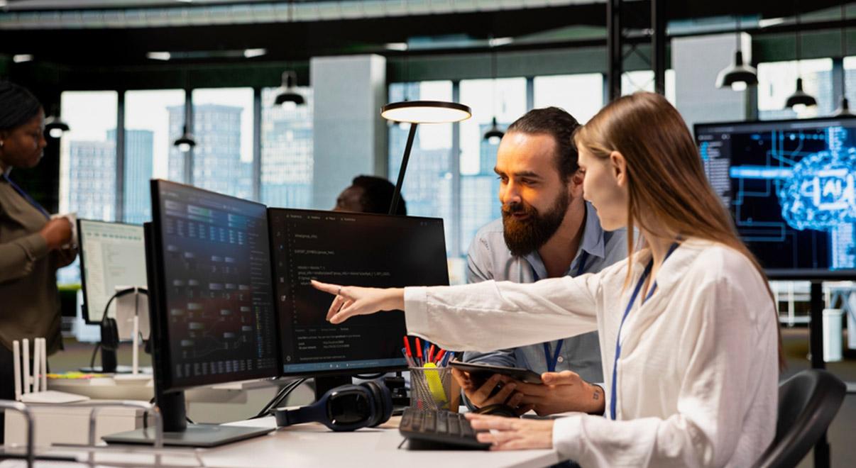 Colleagues collaborating at desks, reviewing code on computer screens in a modern office.