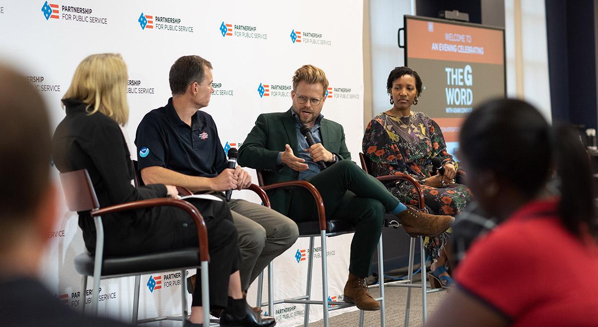 Panel discussion with four speakers on stage at a public service event.