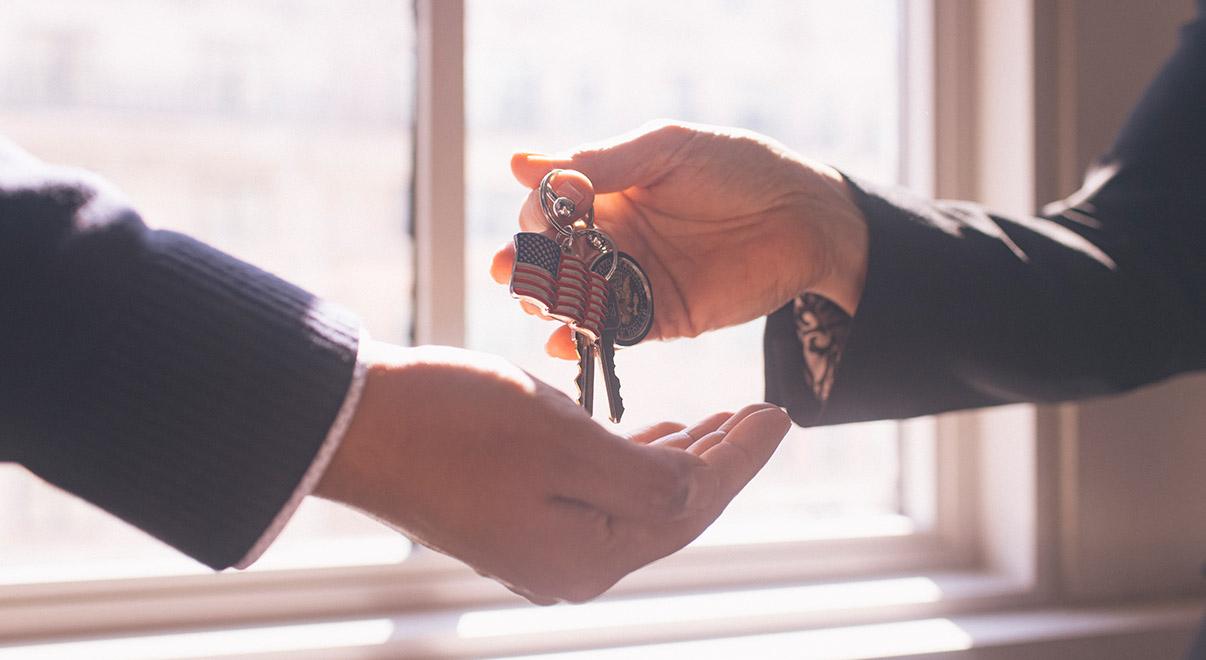 Close-up of one person handing keys with an American flag keychain to another.